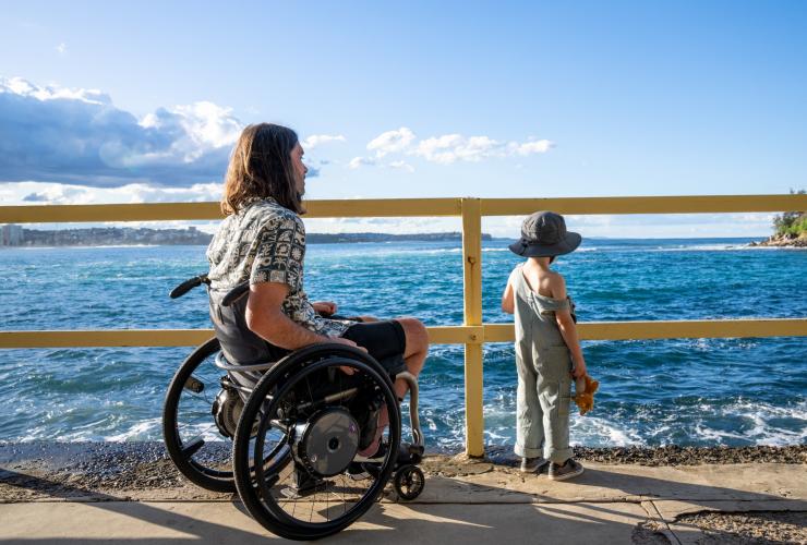 新南威尔士州，悉尼，曼利镇，一位坐轮椅的男子与其儿子一起眺望大海 © 澳大利亚旅游局版权所有