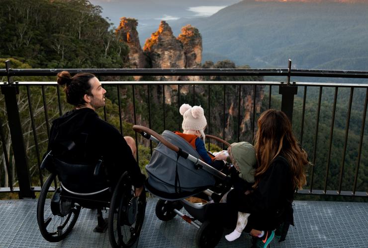 新南威尔士州，蓝山，一位坐轮椅的男子与其爱人和孩子一起眺望三姐妹峰 © 澳大利亚旅游局版权所有
