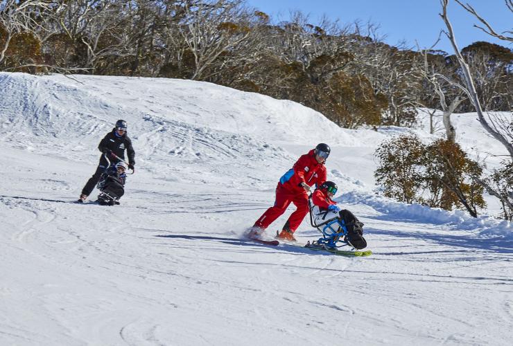 新南威尔士州，大雪山，Thredbo Alpine Village，一名滑雪教练协助适应性滑雪爱好者下山 © 澳大利亚旅游局版权所有