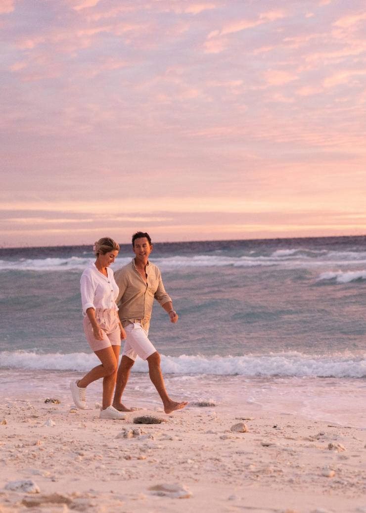 昆士兰州，大堡礁，日落时分在伊利特女士岛生态度假村沿海滩散步的一对男女 © 昆士兰州旅游及活动推广局版权所有