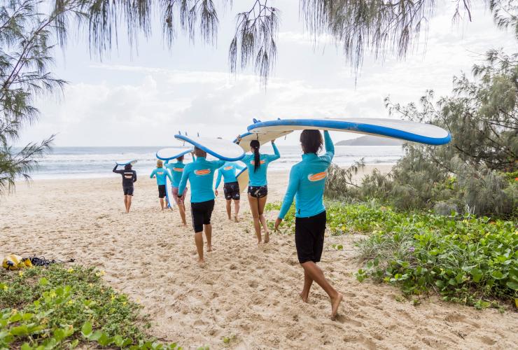 昆士兰州，在努沙，一群人顶着冲浪板踩着金色沙滩走向大海 © 昆士兰州旅游及活动推广局版权所有