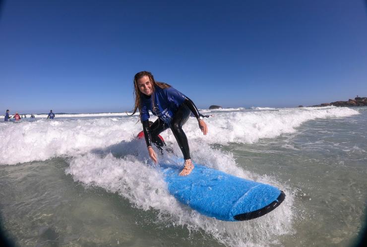 西澳大利亚州，在玛格丽特河的红门海滩，一名女性蹲在冲浪板上，海浪将她带向岸边 © 澳大利亚旅游局版权所有