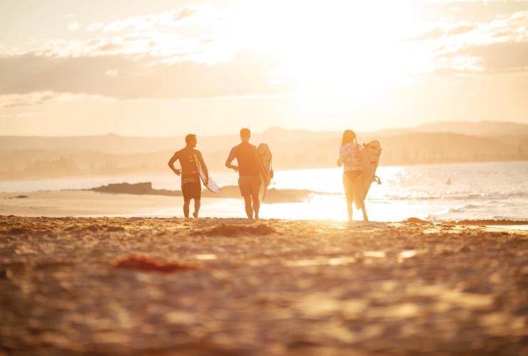 昆士兰州，黄金海岸，三位冲浪者迎着朝阳穿过鲷鱼岩的沙滩奔向大海 © 昆士兰州旅游及活动推广局版权所有