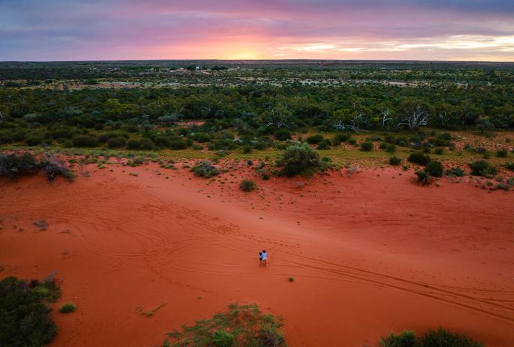 西澳大利亚州，宁加洛，日落时分一对母女在站在 Bullara 牧场一片红色沙地上眺望原始林地的俯视图 © 澳大利亚旅游局版权所有