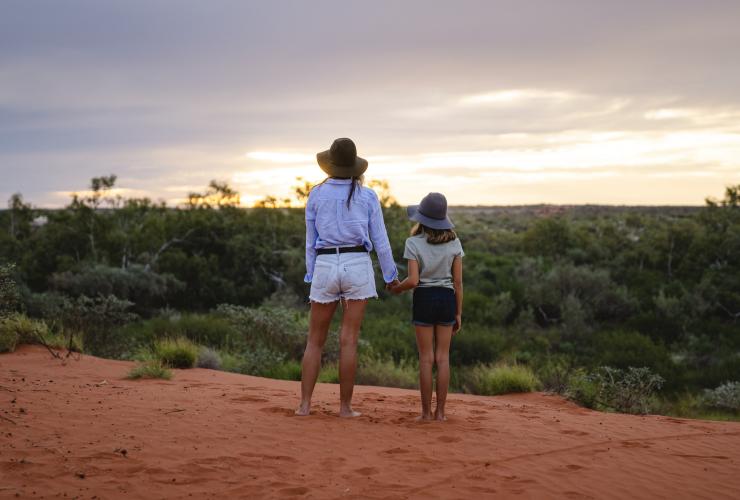 西澳大利亚州，宁加洛，一对母女牵着手站在 Bullara 牧场的红色沙地上俯眺望原始林地 © 澳大利亚旅游局版权所有