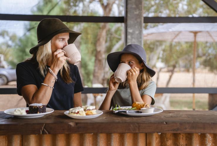 西澳大利亚州，宁加洛，一对母女在 Bullara 牧场享用糕点，用杯子喝水，身后是原始林地 © 澳大利亚旅游局版权所有