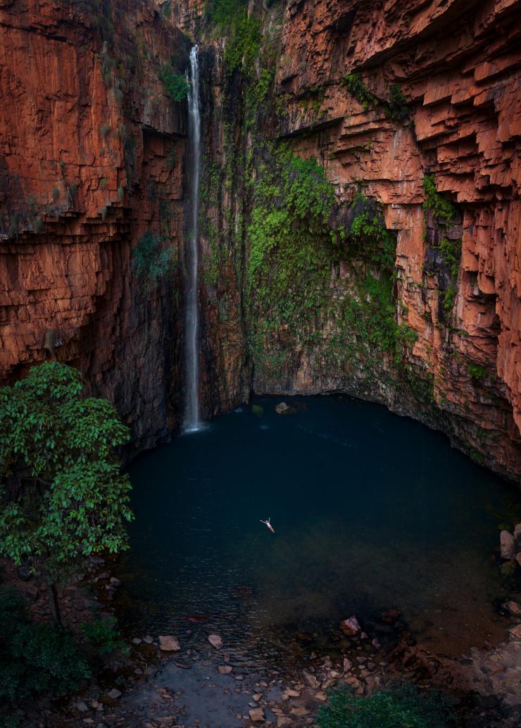 西澳大利亚州，金伯利，一个人漂浮在埃尔奎斯特荒野公园埃玛峡谷深蓝色的水面上，周围是瀑布和红岩悬崖 © 澳大利亚旅游局版权所有