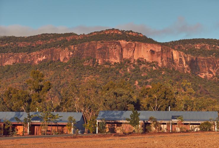 昆士兰州，被树木环绕的穆里根山旅舍建筑外围，背景是穆里根山崎岖的红色山体 © 穆里根山旅舍版权所有
