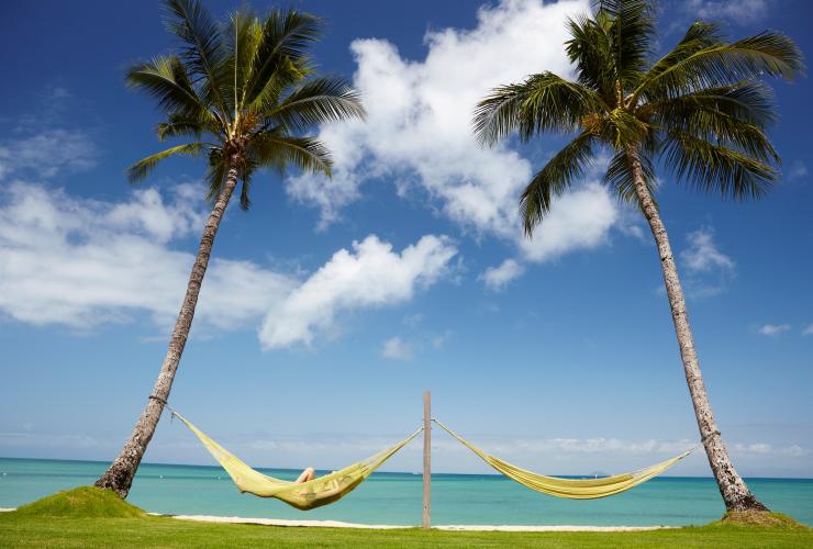 昆士兰州，奥费斯岛旅舍，一个人躺在棕榈树间两张吊床的其中一张上休息，眺望奥费斯岛清澈蔚蓝的海岸线 © 澳大利亚旅游局版权所有