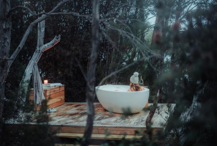 塔斯马尼亚州，圣克莱尔湖，泵房角，一位女士在 The Retreat 别墅的树丛中享受户外浴缸 © Emilie Ristevski 版权所有