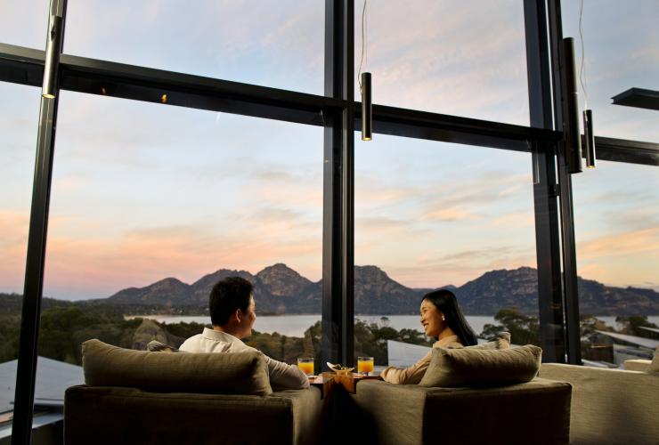 塔斯马尼亚州，日落时分，一对情侣坐在赛菲尔菲欣纳酒店的休闲椅上，远处是歌斯湾的山水美景 © Myka Photography 版权所有